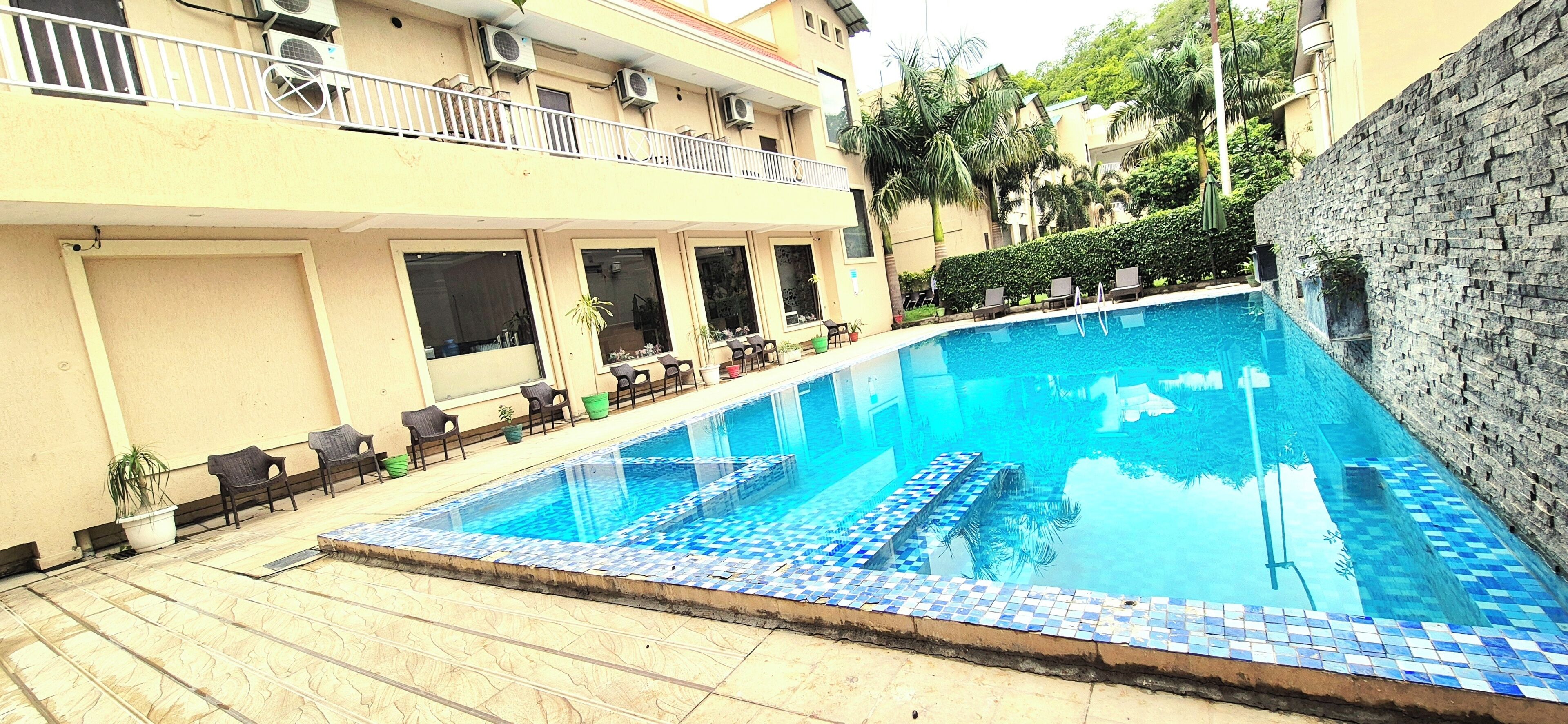 A swimming pool with tiled edges, surrounded by a building with balconies and potted plants.