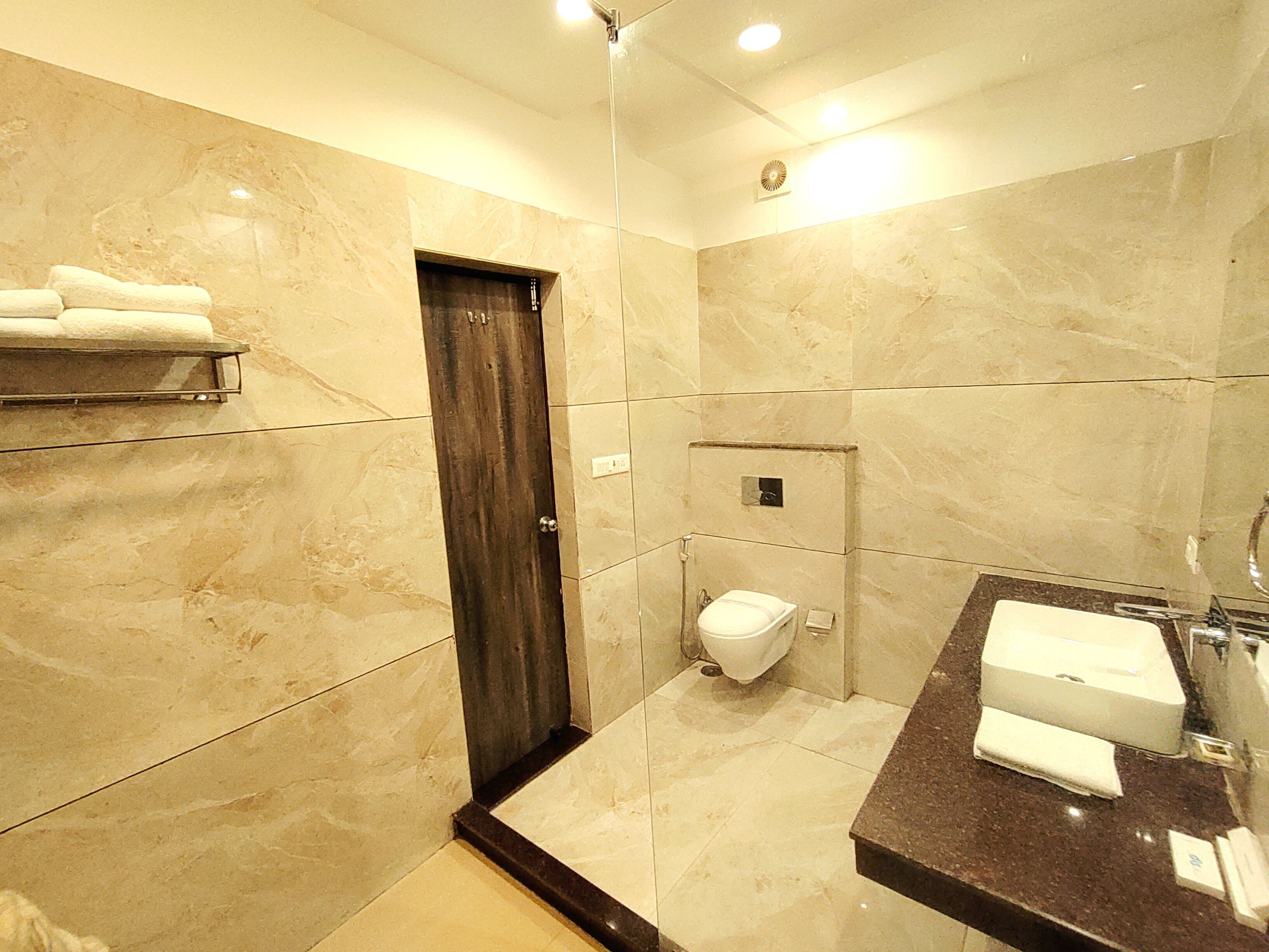 A bathroom with a marble floor, a dark wooden door, a white toilet, a sink with a mirror, and a towel rack.