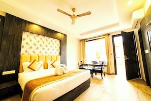 A hotel room with a bed, a ceiling fan, a dining table, and a view of the outdoors. - La Savanna Resort And Spa By DL Hotels And Resorts (Ramnagar)