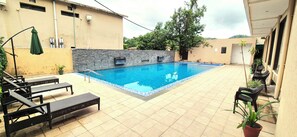 A swimming pool with lounge chairs, a stone wall, and potted plants. - La Savanna Resort And Spa By DL Hotels And Resorts (Ramnagar)