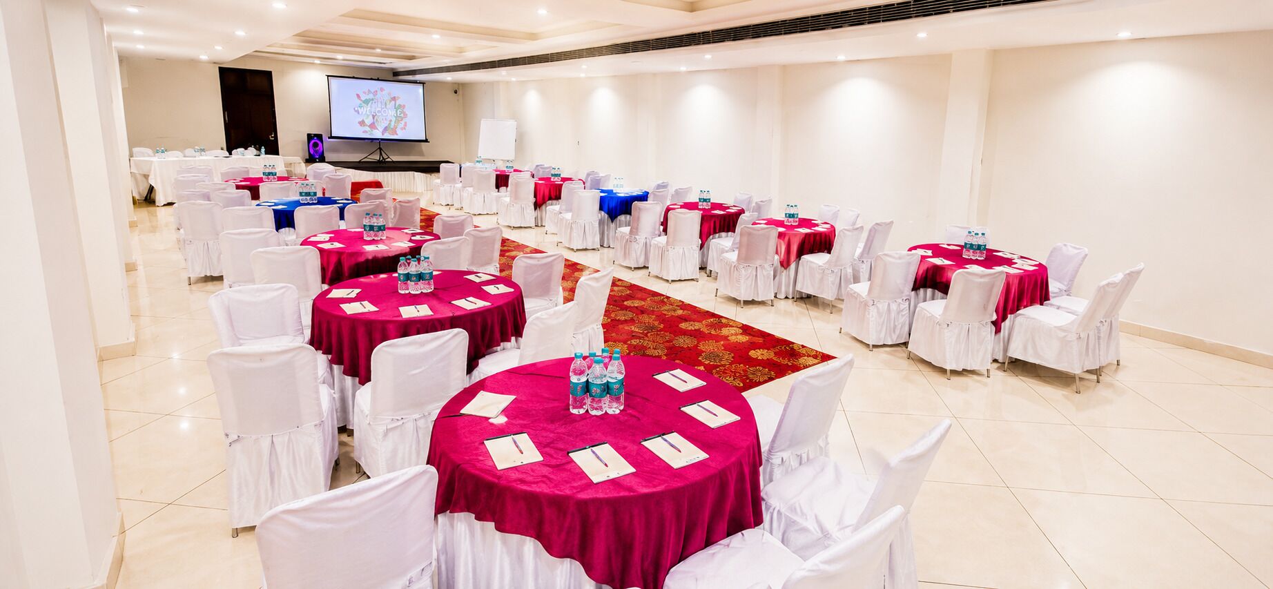 A conference room with round tables, white chairs, and a projector screen.