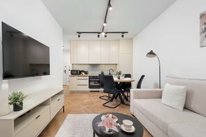 A modern living room with a flat-screen TV, a sofa, a coffee table, and a dining area with chairs and a table. - Charming Apartment with a Terrace | Pets Welcome (Łódź)