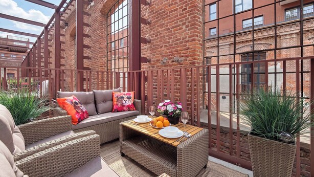 Un espace patio aménagé avec des meubles en osier, une table avec des assiettes et des verres, et des plantes en pot.