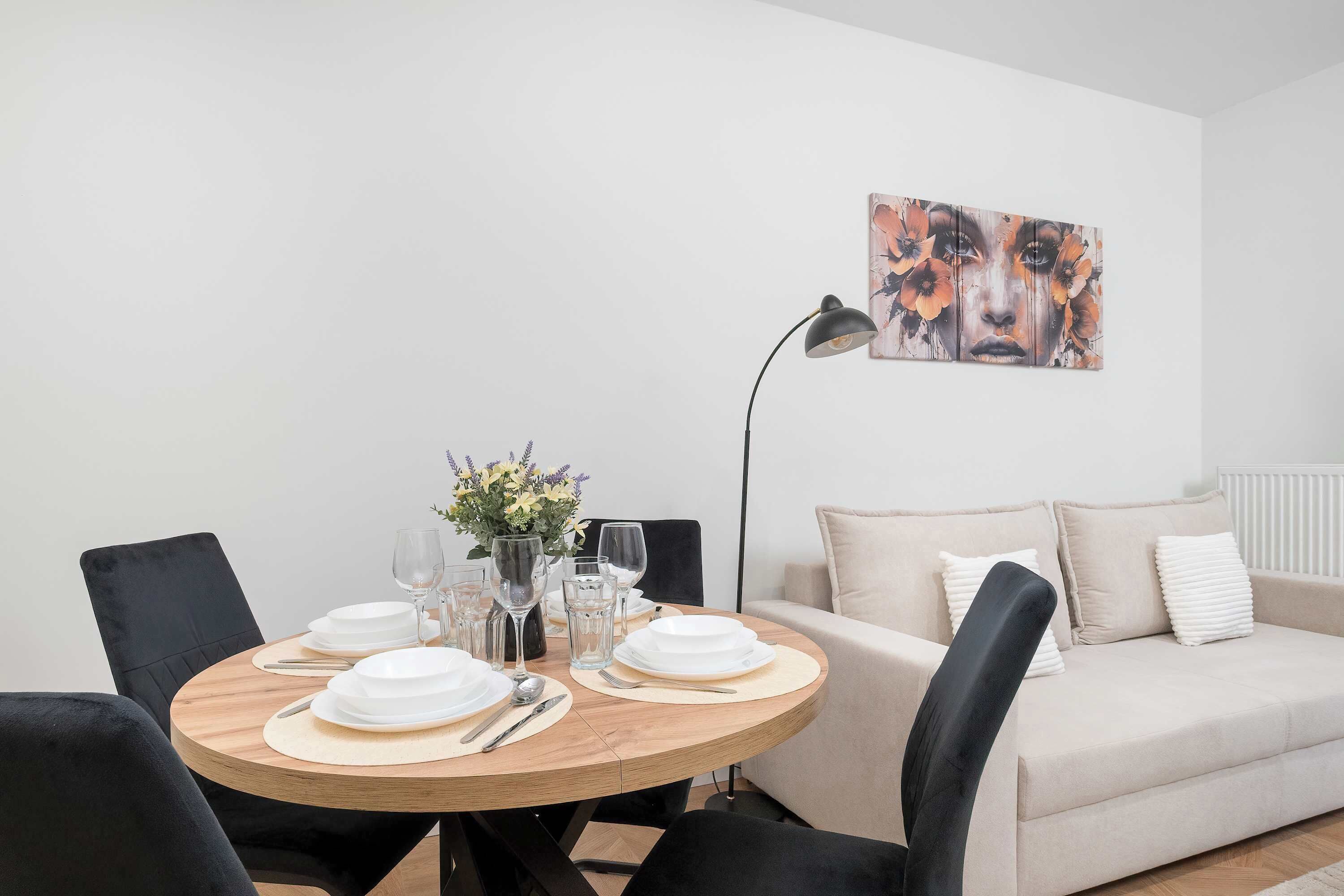 Un coin repas avec une table ronde en bois, dressée pour quatre personnes, un canapé et un tableau accroché au mur.