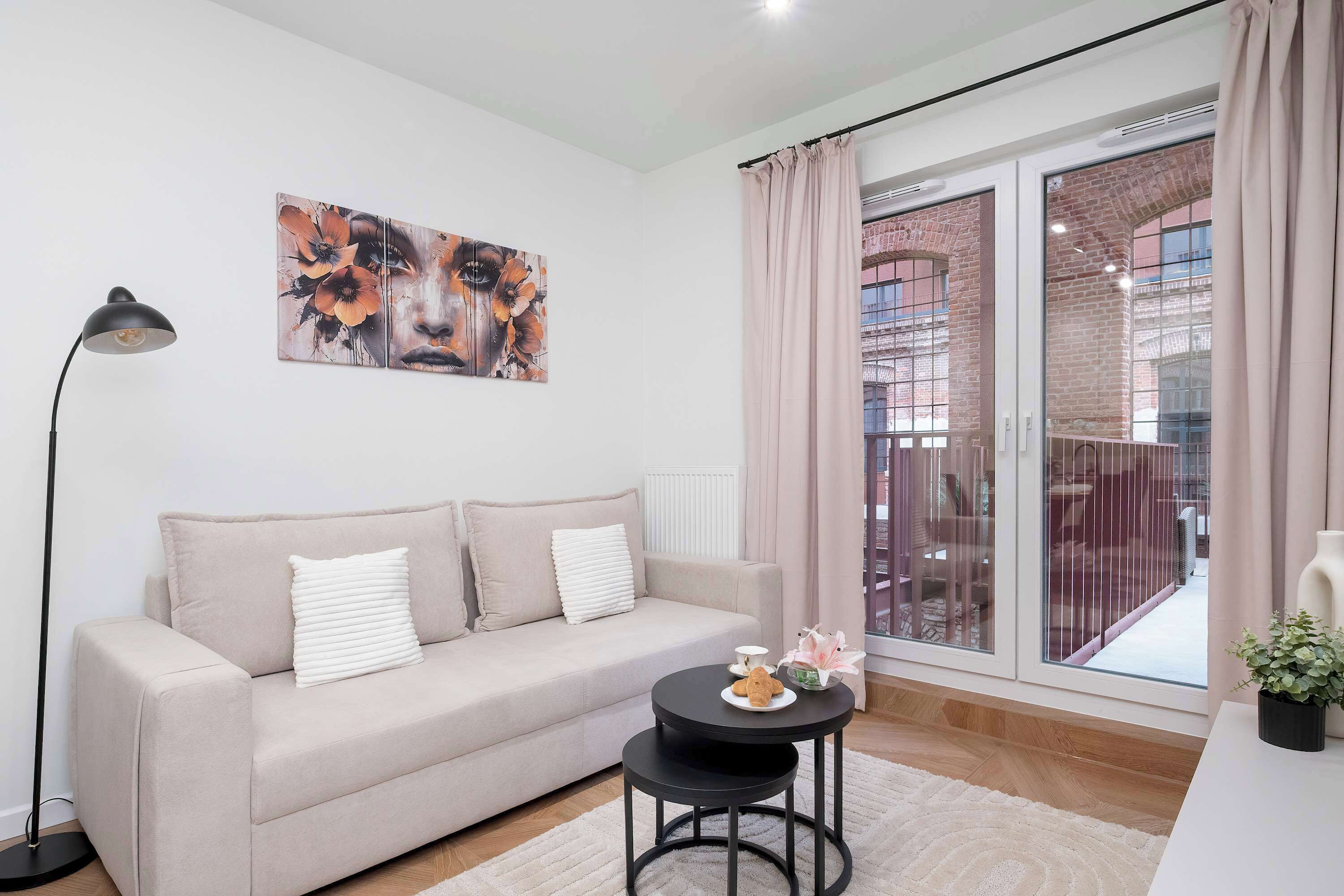A living room with a sofa, a small round table, a floor lamp, and a large window with curtains.