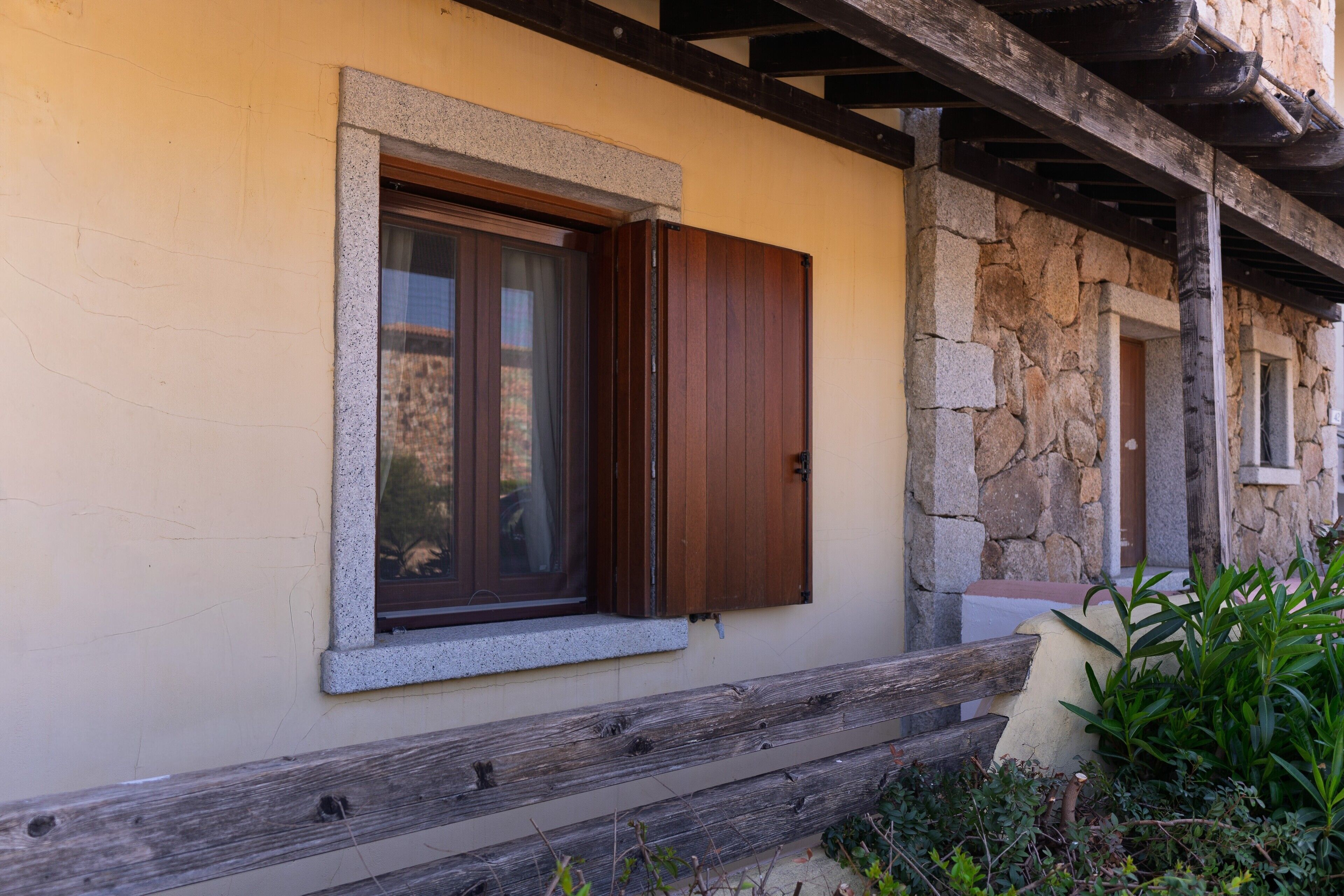 A building with a stone wall, a wooden bench, and a window with a wooden shutter.