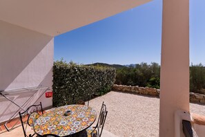 Eine Terrasse mit einem runden Tisch und Stühlen, einem Wäscheständer aus Metall und einer Hecke.