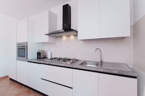 Eine moderne Küche mit weißen Schränken, einer Edelstahl-Spüle, einem Gasherd und einem eingebauten Backofen.