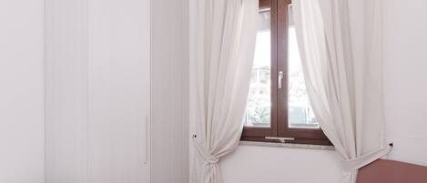 Una habitación con cama, armario, cortinas en la ventana y una silla.