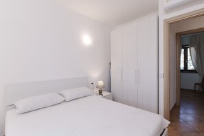 Ein Schlafzimmer mit Bett, Nachttisch, Lampe, Kleiderschrank und einer Tür zu einem anderen Raum.