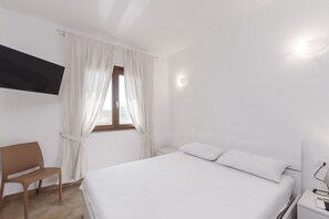 Ein Schlafzimmer mit einem Bett, einem Sessel, einem an der Wand montierten Fernseher und einem Fenster mit Vorhängen.