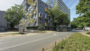 Un edificio de varios pisos con un logo destacado en la fachada, balcones y una vista de la calle con coches estacionados.