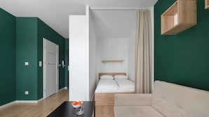 Una habitación moderna con una cama, un sofá, una mesa con naranjas y un vaso, y un estante de madera.