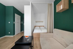 Ein modernes Zimmer mit einem Bett, einer Couch, einem Tisch mit Orangen und einem Glas sowie einem Holzregal.