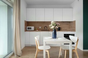 Eine moderne Küche mit weißen Schränken, einer Holzwand und einem Esstisch mit Stühlen, dazu ein Blumenstrauß in einer Vase.