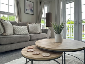 Ein Wohnzimmer mit grauem Sofa, einem runden Holztisch und einer Topfpflanze.