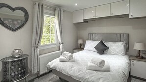 Une chambre à coucher avec un lit, des tables de chevet, une commode, un miroir et une fenêtre avec des rideaux.