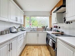 A kitchen with white cabinets, a built-in oven, a washing machine, and a window with a view of greenery. - 2 bedroom accommodation in Paignton (Paignton)
