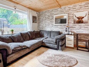 A modern living room with a sectional sofa, a round rug, a stone wall, and a framed picture of a bull. - 2 bedroom accommodation in Paignton (Paignton)