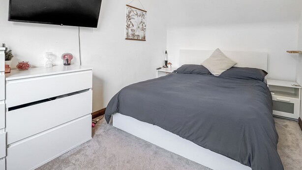 Una camera da letto con un letto, una TV fissata al muro, un comodino con una lampada e un piccolo oggetto decorativo sul comò.