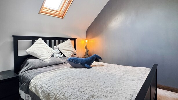 A bedroom with a sloped ceiling, a skylight, a bed with pillows, a plush toy, and a bedside lamp. - 2 bedroom accommodation in Paignton (Paignton)