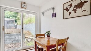 Zona pranzo con tavolo e sedie in legno, una pianta in vaso, una mappa del mondo appesa al muro e una porta scorrevole in vetro che dà sull'esterno.