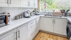Una cucina con mobili bianchi, un tostapane, una macchina per il caffè e una finestra vista sul verde.