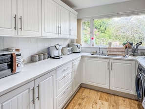 A kitchen with white cabinets, a toaster, a coffee maker, and a window with a view of greenery. - 2 bedroom accommodation in Paignton (Paignton)