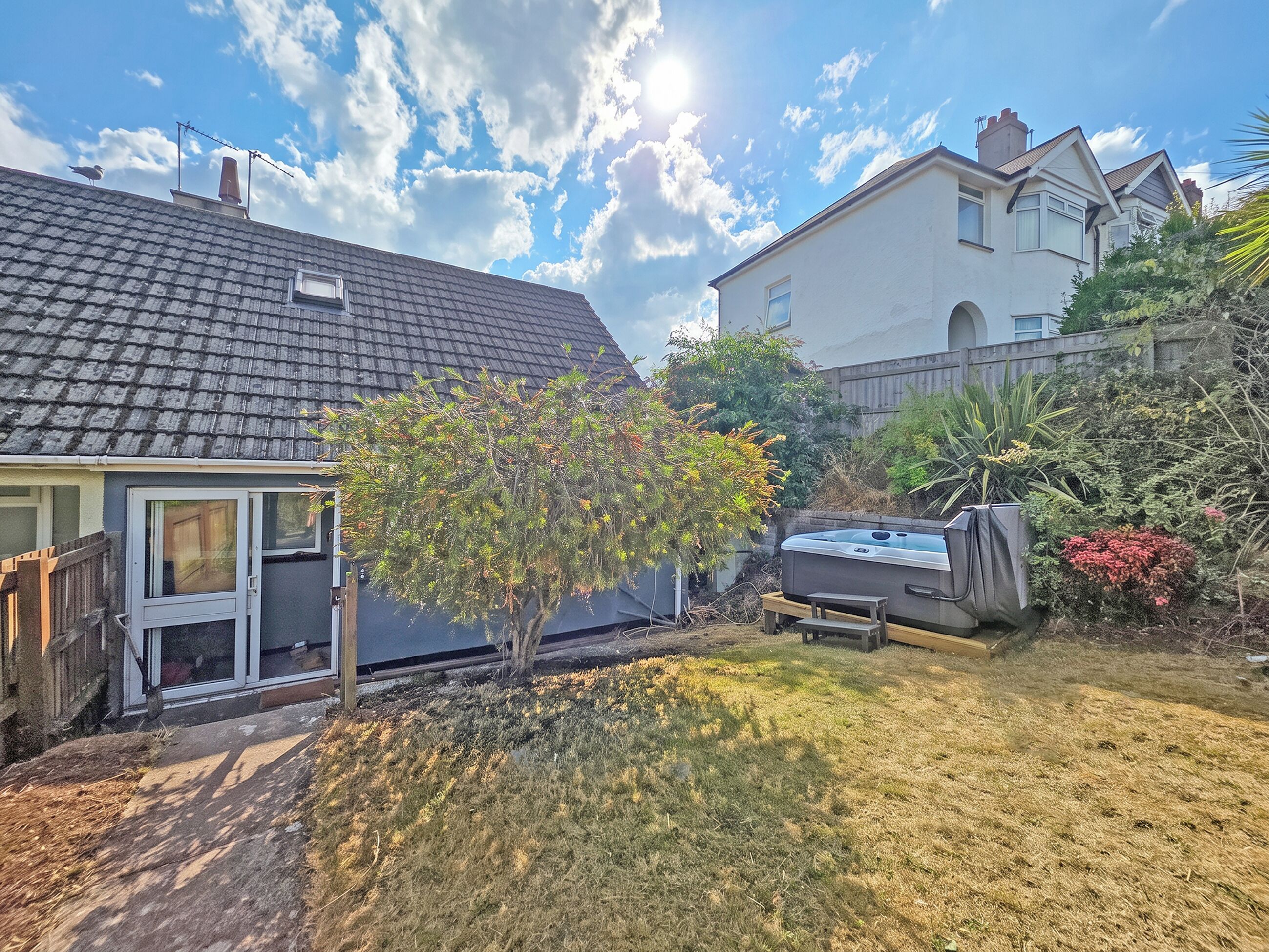 Un jardin à l’arrière d’une maison, avec un arbre, un jacuzzi et une maison dont le toit est recouvert de tuiles.