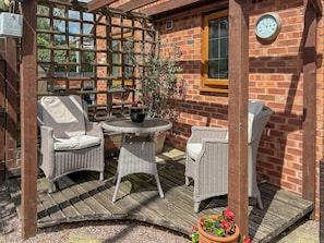 A wooden pergola with wicker furniture, a brick wall, and a clock.