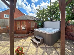 Un jacuzzi en un patio trasero con una terraza de madera, una casa de ladrillo y una pérgola.