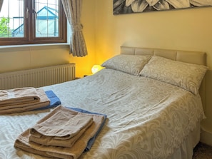 Una cama bien hecha con ropa de cama estampada, una ventana con cortinas, un radiador y una lámpara.