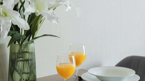 Une table à manger ornée d’un vase de fleurs blanches, de deux verres de jus d’orange et d’assiettes.