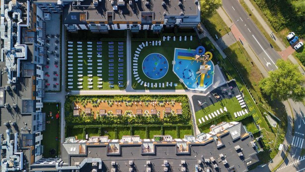 Vue aérienne d’un bâtiment moderne doté d’un jardin sur le toit, d’une piscine et d’un parking.