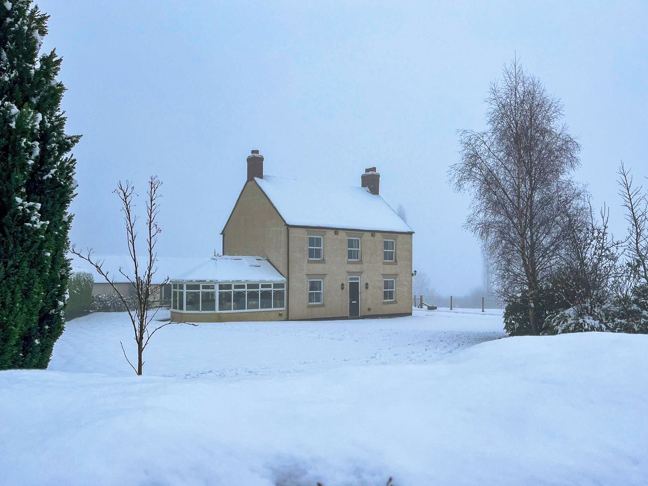 Une maison à deux étages, dont le toit est recouvert de neige, et qui possède une véranda.