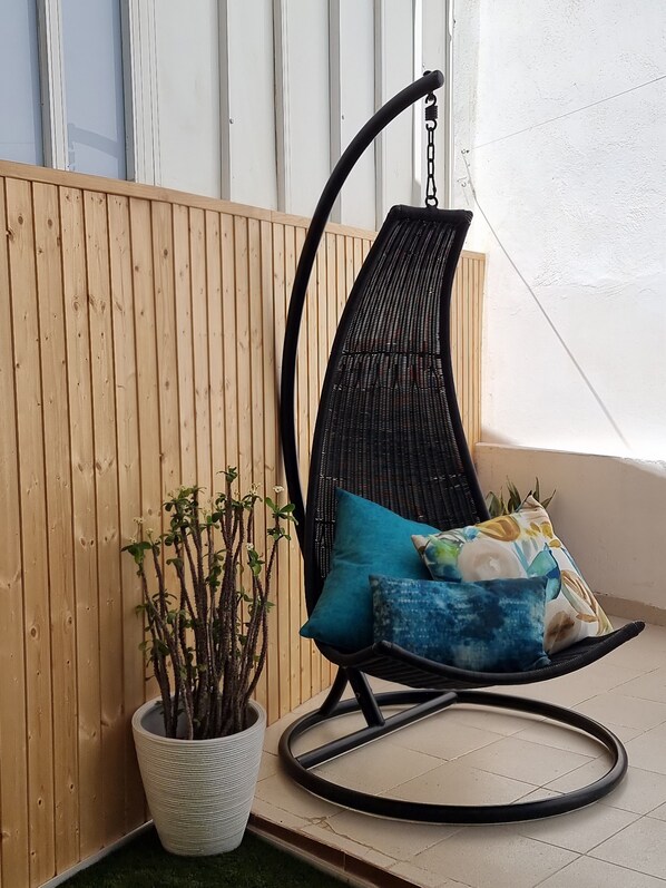 Una silla colgante con cojines, una planta en maceta y un panel de madera.