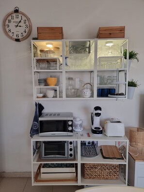 Una cocina con un reloj, microondas, tostadora y diversos utensilios de cocina en estantes.