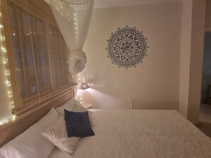 Un dormitorio con cama, un diseño decorativo en la pared, una lámpara de noche y una ventana con cortina.