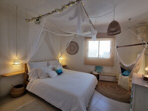 Een slaapkamer met een hemelbed, hangstoelen, een bedlampje en een decoratieve wandversiering.