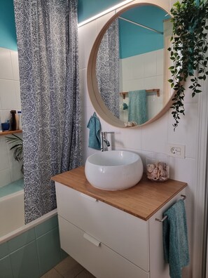 Un baño con un lavamanos blanco, un espejo redondo, una toalla azul y una cortina de ducha estampada.