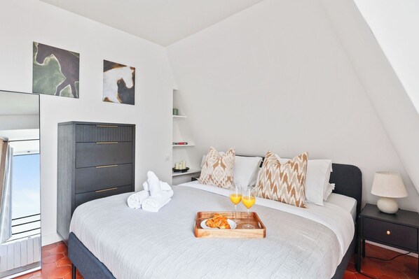 A bedroom with a bed, bedside table, and a tray with food and drinks. - Charming 1BR Hidden Gem in Le Marais (Paris)