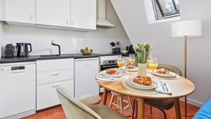 Et moderne køkken med hvide skabe, en sort bordplade og et spiseområde med et bord dækket til morgenmad.