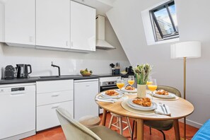 A modern kitchen with white cabinets, a black countertop, and a dining area with a table set for breakfast. - Charming 1BR Hidden Gem in Le Marais (Paris)