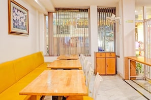 A hotel room with a yellow sofa, wooden tables, a cabinet, and a window with vertical blinds.
