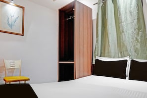 A bedroom with a bed, a wooden wardrobe, a chair, and a painting on the wall.