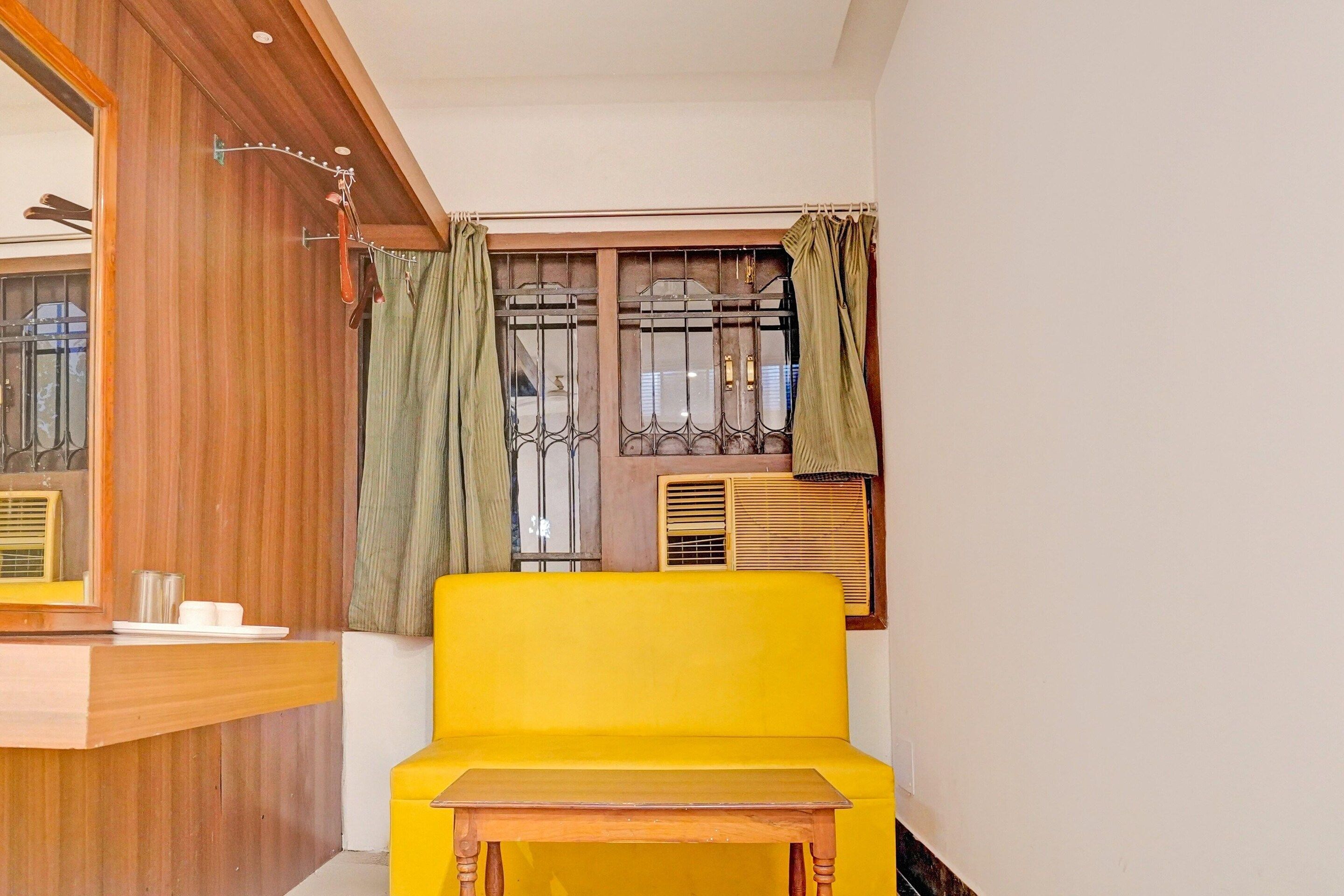A room with a yellow sofa, a wooden table, a window with metal bars, and a curtain.