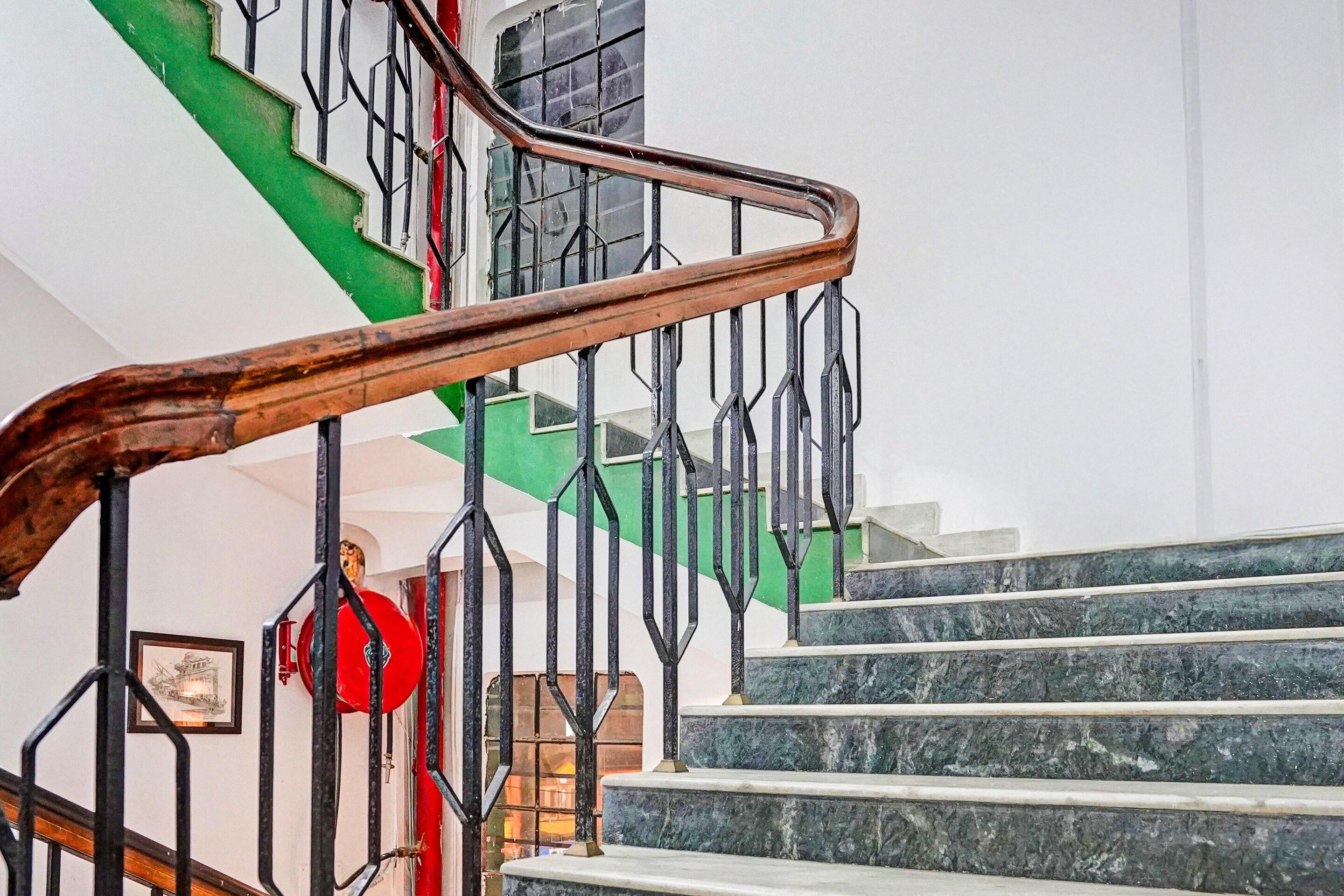 Un escalier avec une main courante en bois et des rampes en métal noir, menant à un palier où se trouve un ballon rouge.