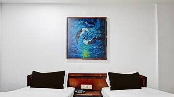 A hotel room with two beds, a painting on the wall, and a wooden headboard.