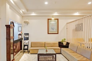 A living room with a sofa, a coffee table, a clock, a fan, a framed picture, and a newspaper rack.