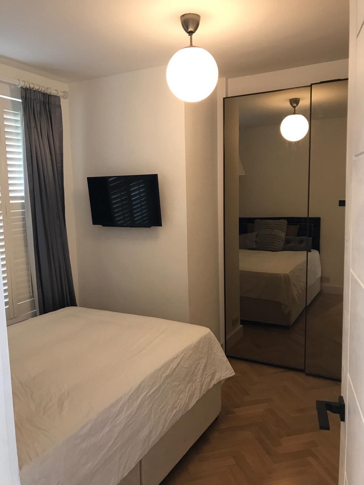 A bedroom with a bed, a TV mounted on the wall, a mirror, and a ceiling light.